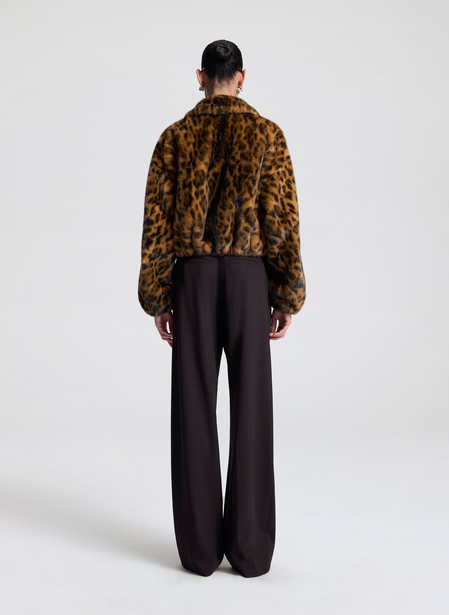 Person wearing a leopard print jacket and black pants on a white background