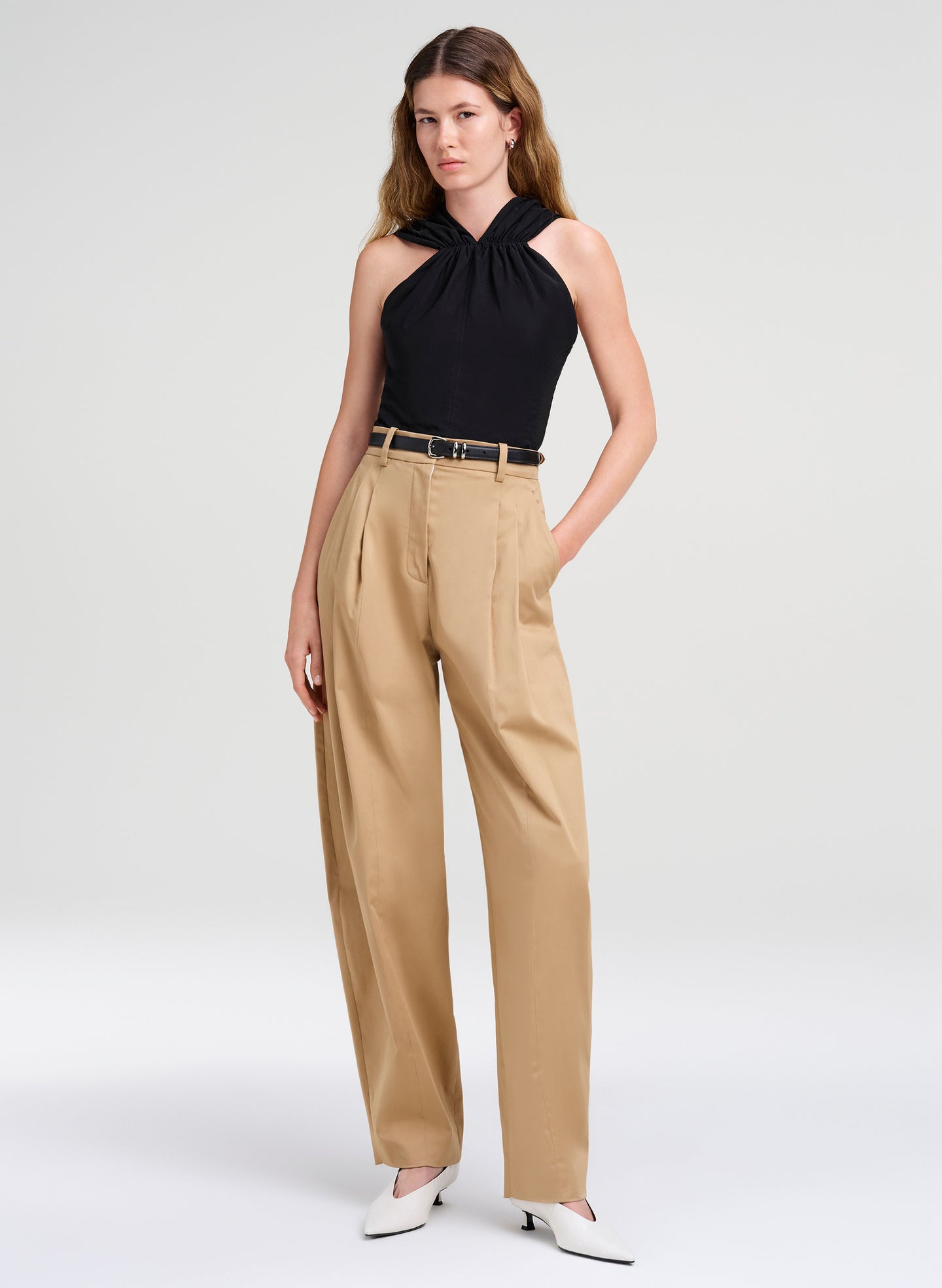Woman wearing a black halter top and beige high-waisted pants on a white background