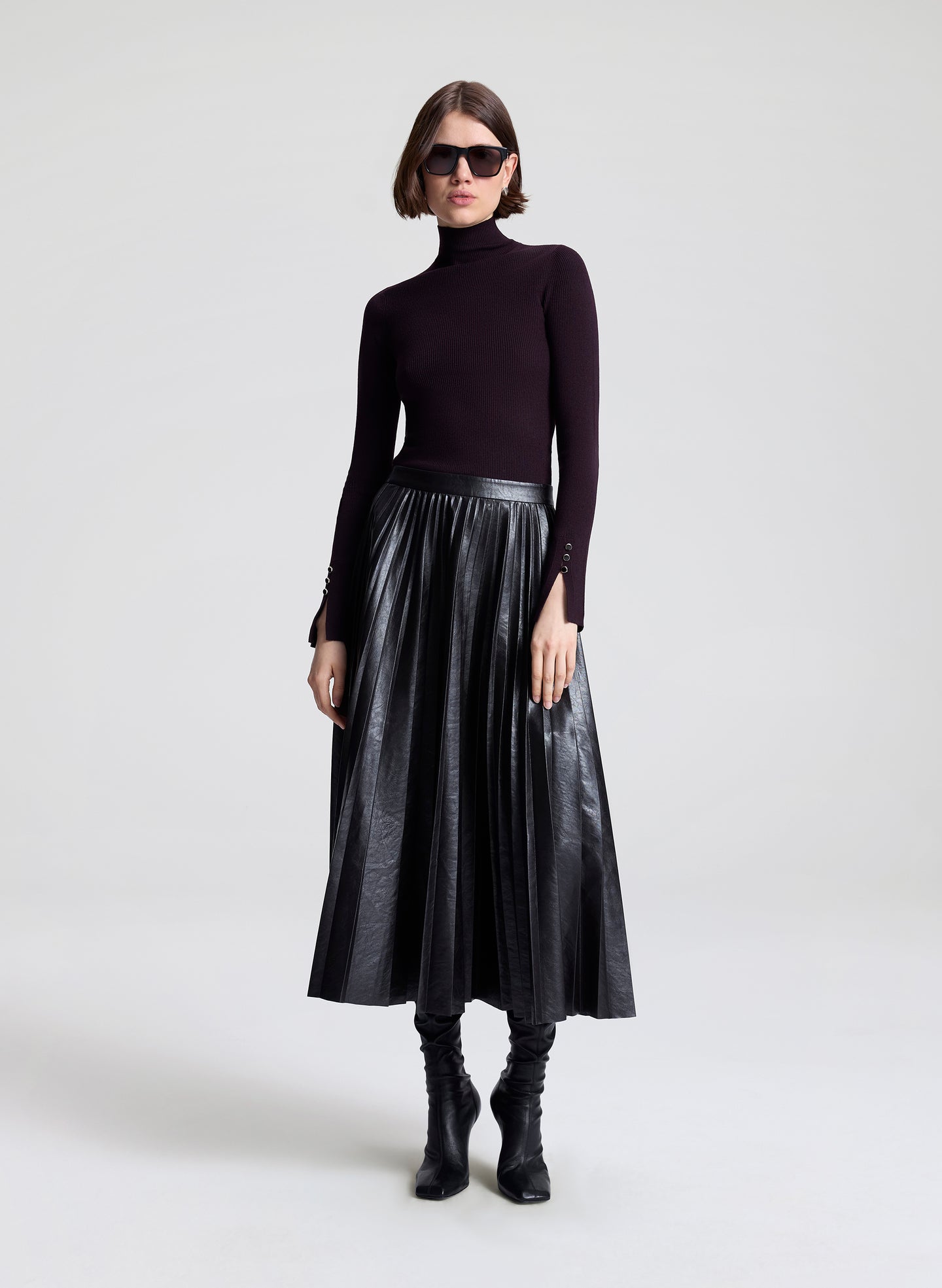 Woman wearing a black turtleneck, metallic skirt, and black boots on a white background