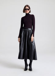 Woman wearing a black turtleneck, metallic skirt, and black boots on a white background