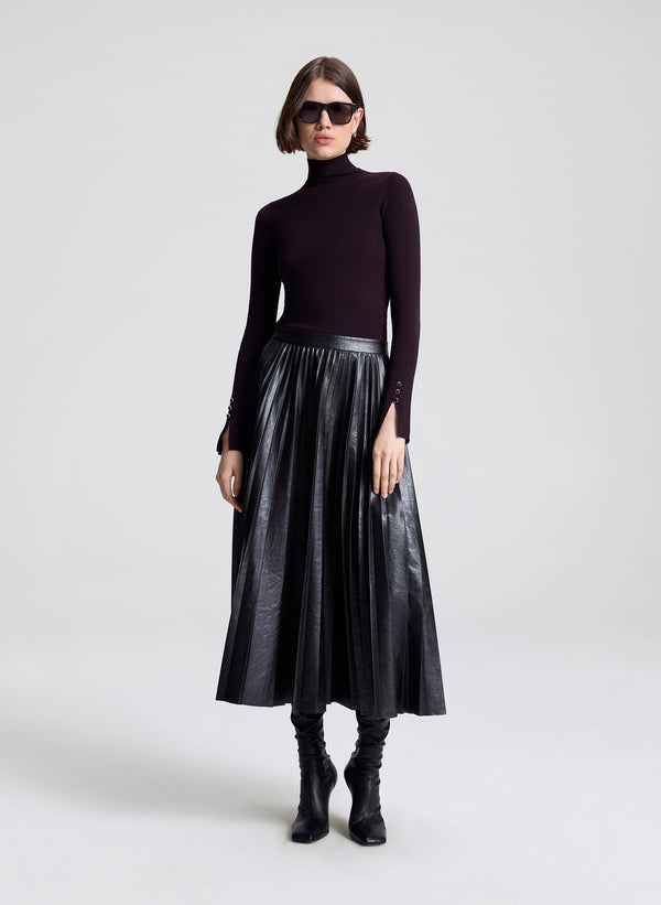 Woman wearing a black turtleneck, metallic skirt, and black boots on a white background