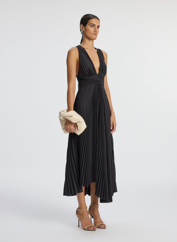 Side view of woman wearing black deep v-neck pleated midi dress