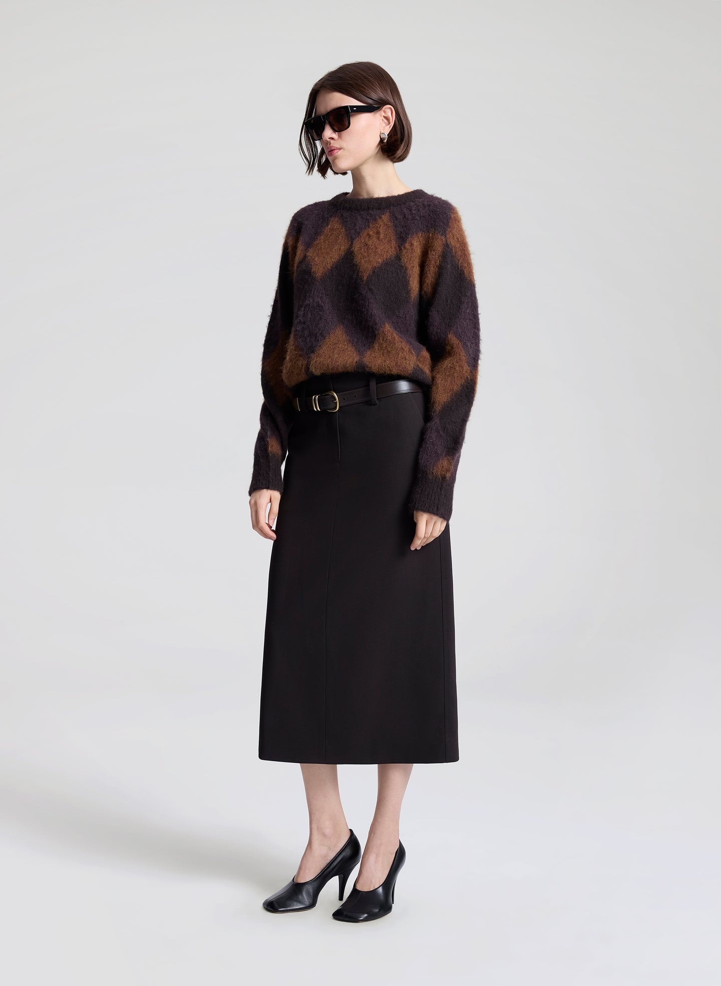 Person wearing a brown and black checkered sweater with a black skirt on a white background