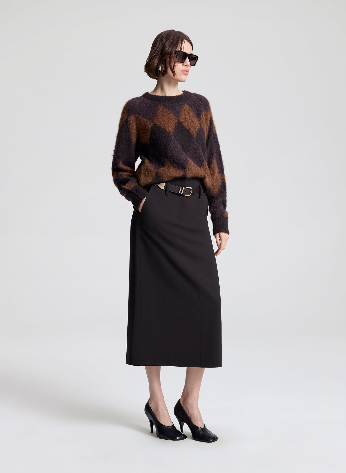 Woman wearing a patterned sweater and black skirt on a white background