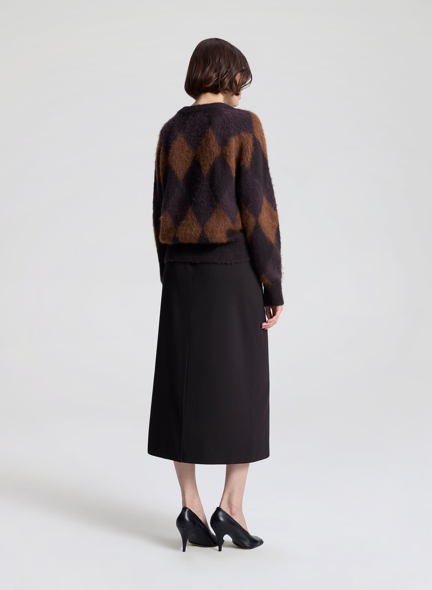 Person wearing a patterned sweater and black skirt on a white background