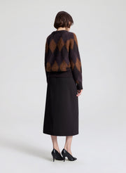 Person wearing a patterned sweater and black skirt on a white background