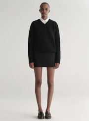 Person wearing a black sweater over a white shirt and a black mini skirt on a plain background