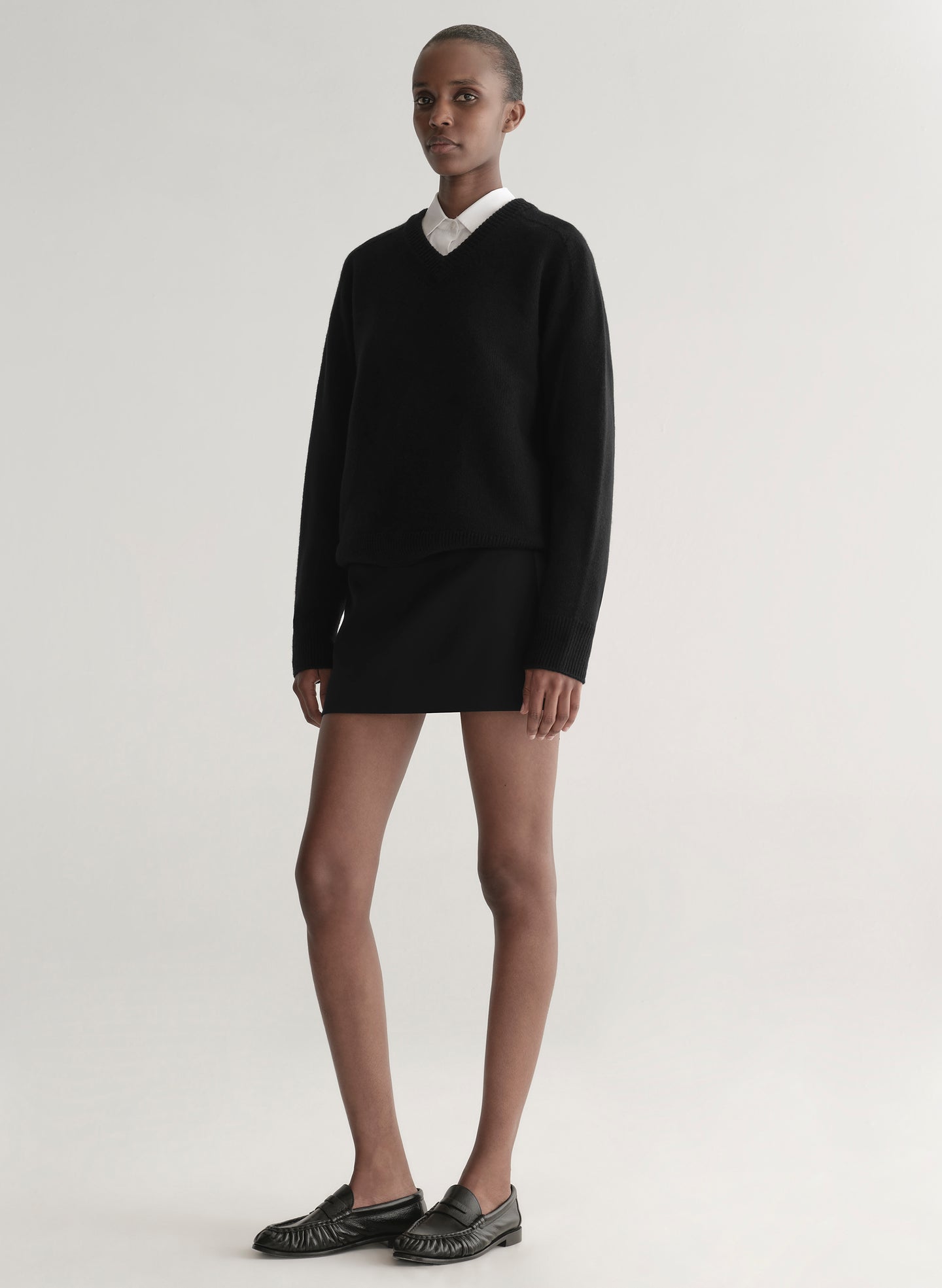 Person wearing a black sweater over a white shirt and a black mini skirt on a plain background