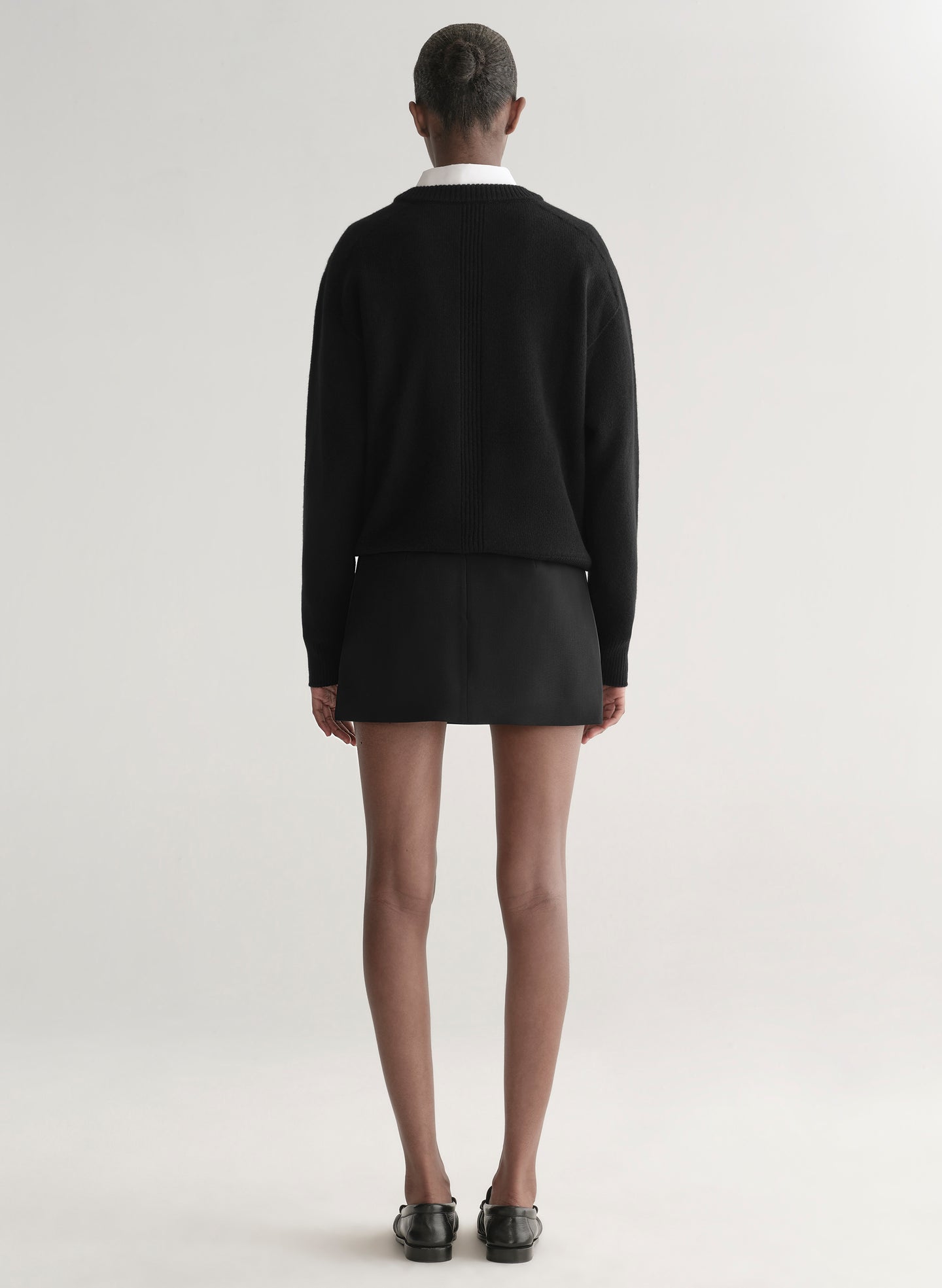 Person wearing a black sweater over a white shirt and a black mini skirt on a plain background