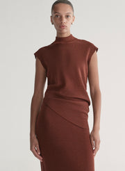 Woman wearing a rust colored sleeveless top and skirt set against a plain background