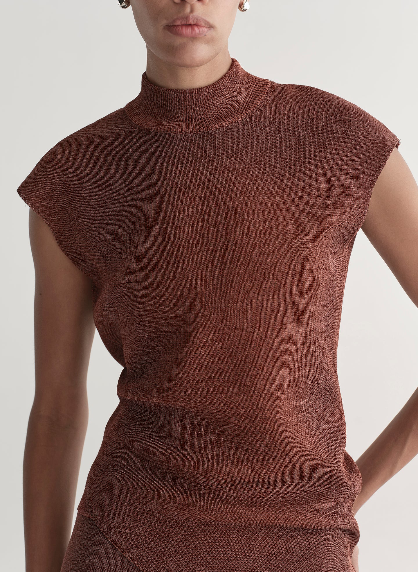 Woman wearing a rust colored sleeveless top and skirt set against a plain background