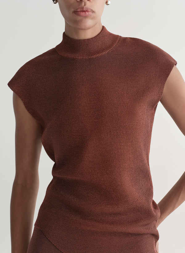 Woman wearing a rust colored sleeveless top and skirt set against a plain background