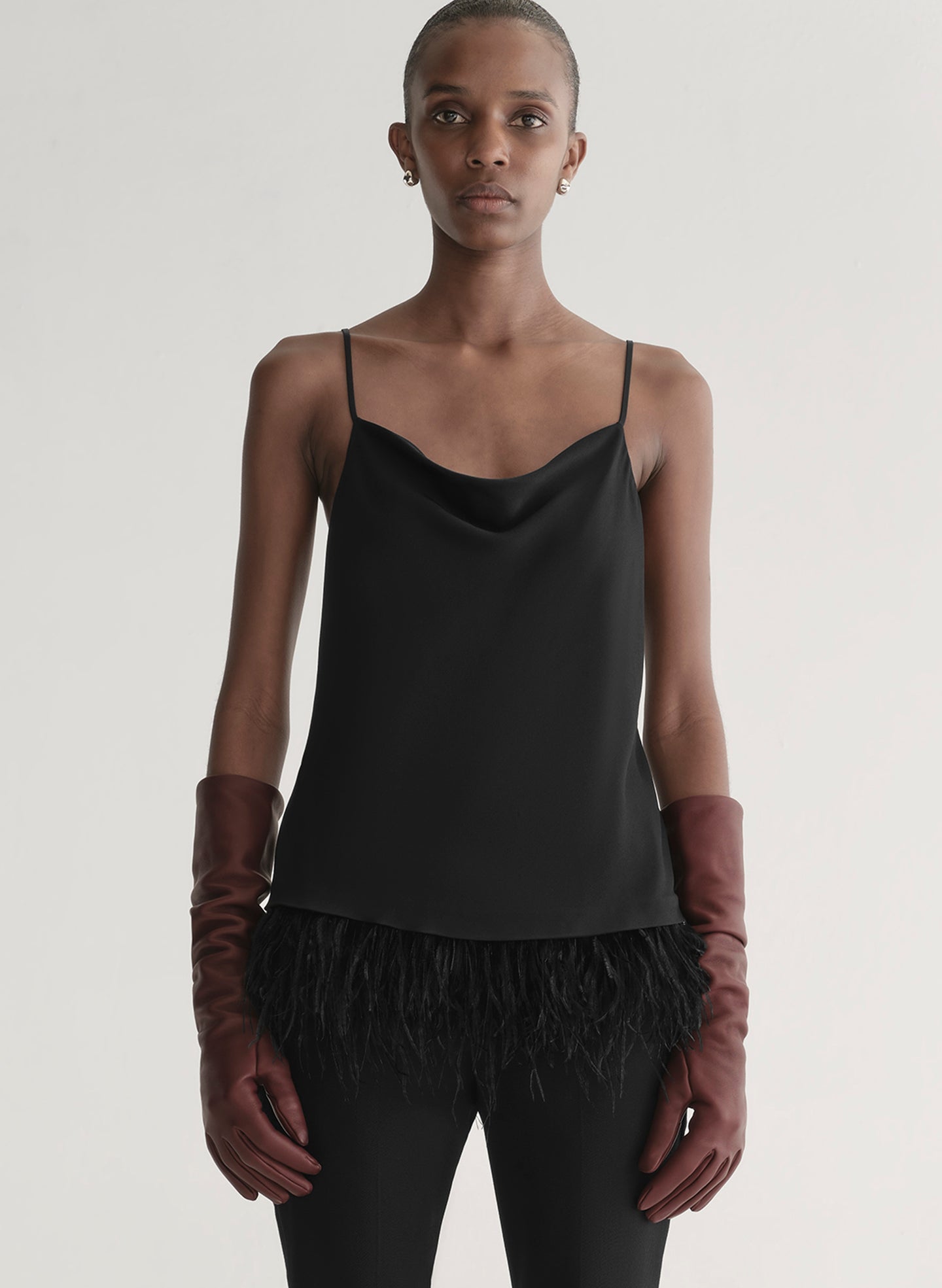 Woman wearing a black slip top with feathered hem and red gloves on a plain background