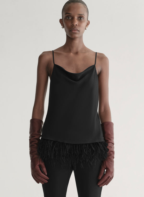 Woman wearing a black slip top with feathered hem and red gloves on a plain background