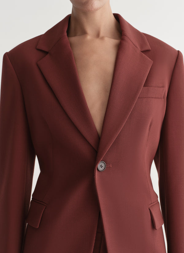 Woman wearing a maroon suit against a plain background