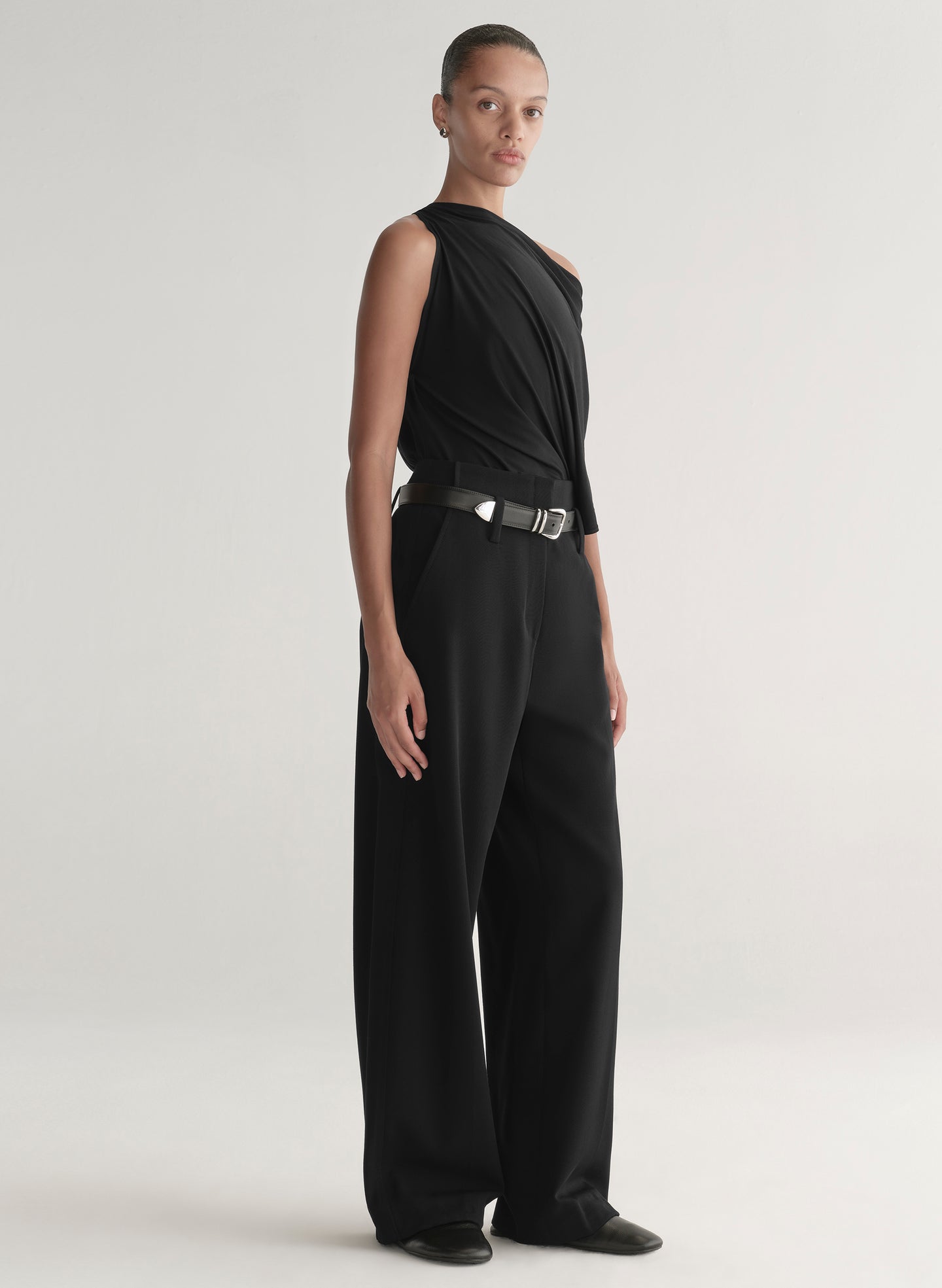 Woman wearing a black one-shoulder top and black pants on a light gray background