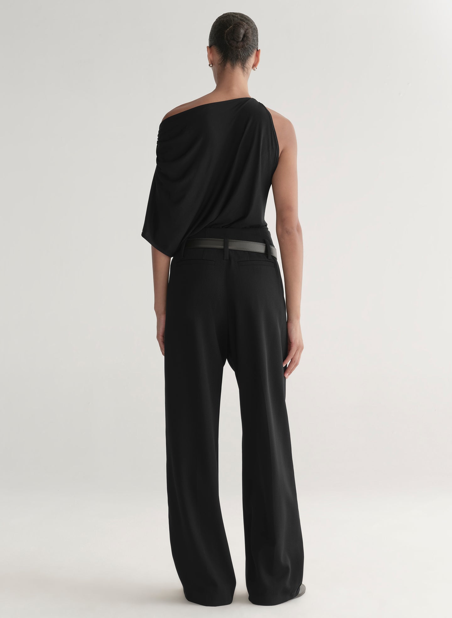 Woman wearing a black one-shoulder top and black pants on a light gray background