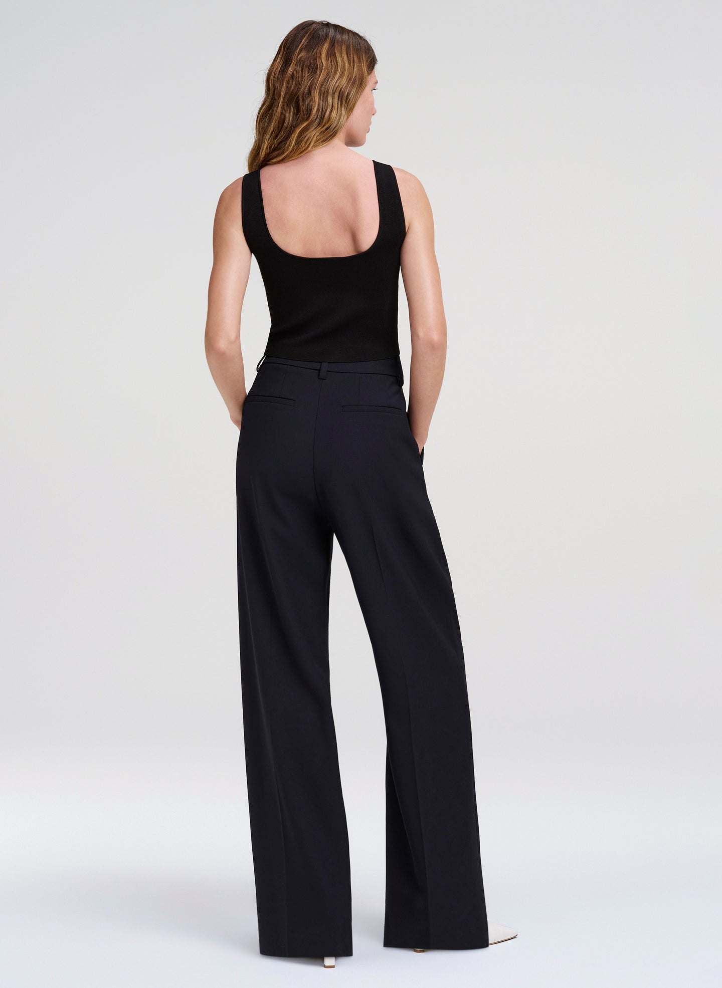 Woman wearing a black sleeveless top and wide-leg pants on a white background