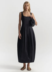 Woman wearing a blue sleeveless dress holding a blue handbag on a white background