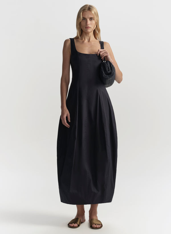 Woman wearing a blue sleeveless dress holding a blue handbag on a white background