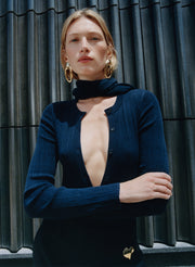 Woman wearing a dark blue cardigan with a deep neckline against a metallic background