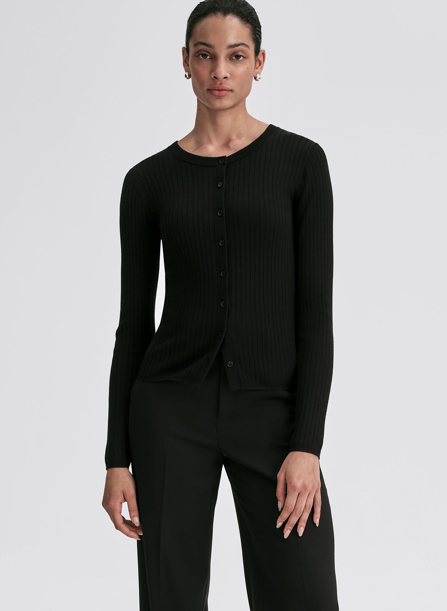 Person wearing a black ribbed long-sleeve cardigan and pants on a light gray background
