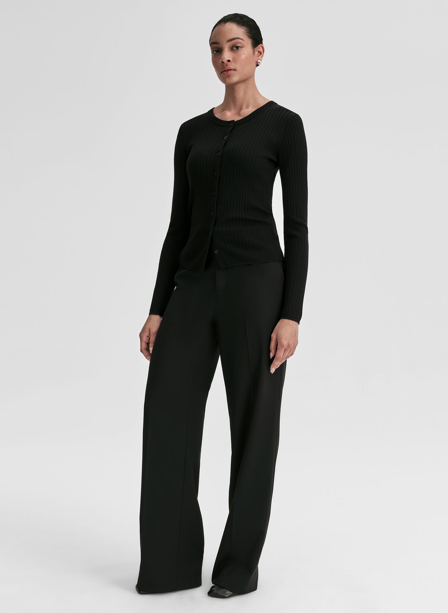 Person wearing a black ribbed long-sleeve cardigan and pants on a light gray background