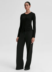 Person wearing a black ribbed long-sleeve cardigan and pants on a light gray background