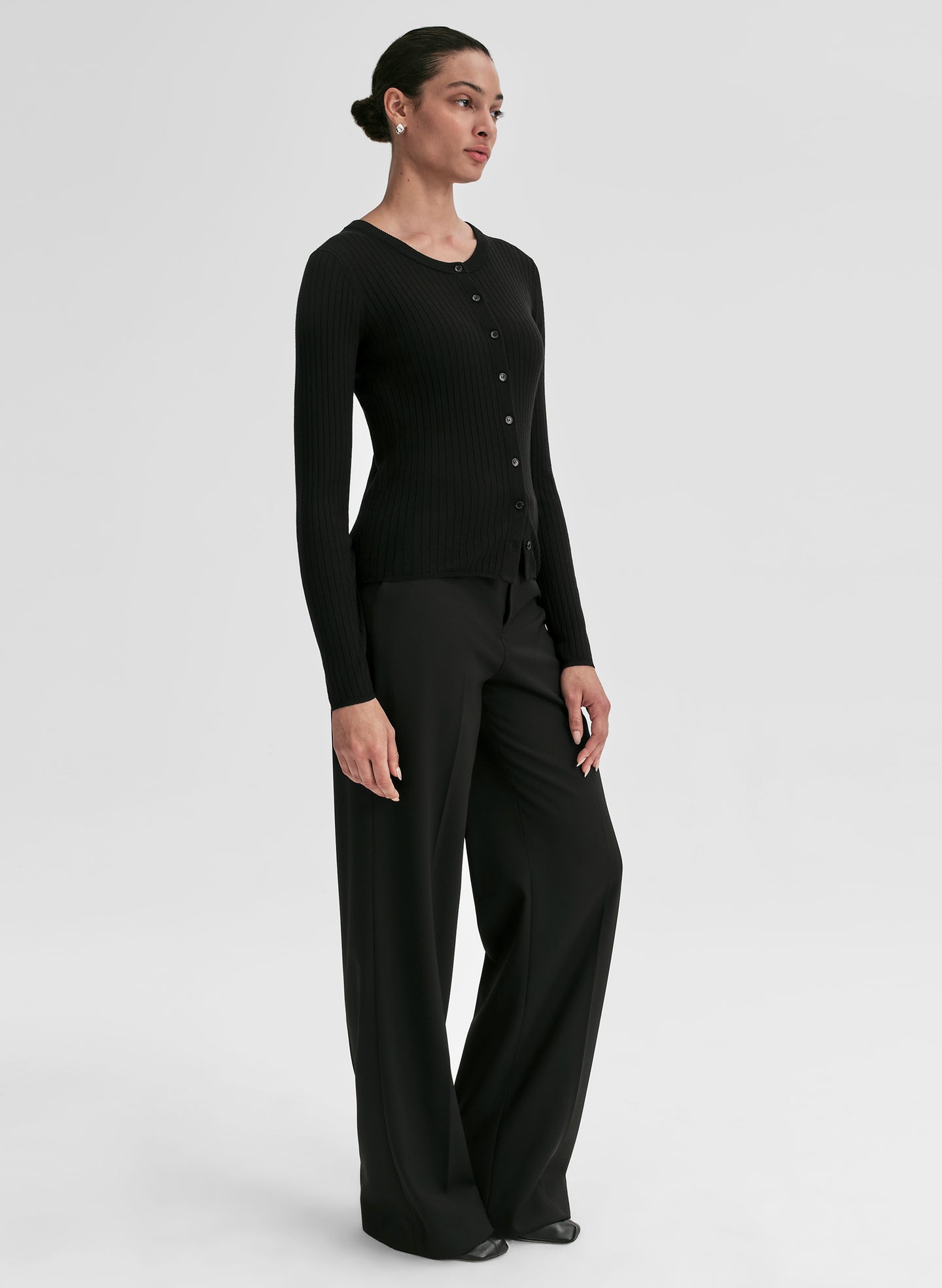 Person wearing a black ribbed long-sleeve cardigan and pants on a light gray background