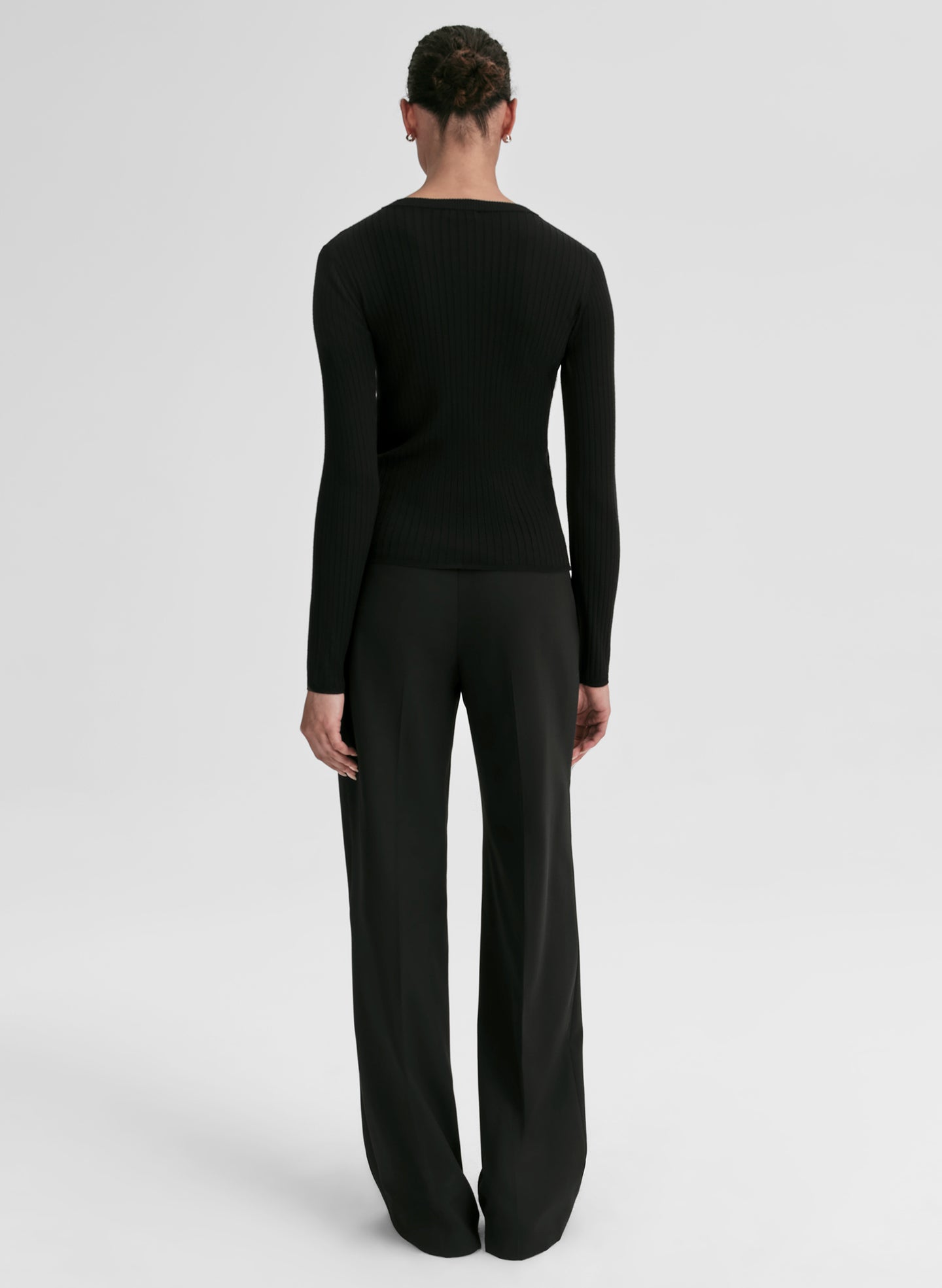 Person wearing a black ribbed long-sleeve cardigan and pants on a light gray background