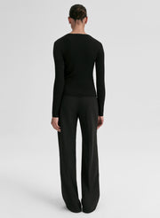 Person wearing a black ribbed long-sleeve cardigan and pants on a light gray background