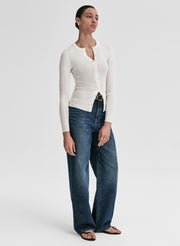 Woman wearing a white ribbed cardigan and blue jeans on a light gray background