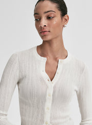 Woman wearing a white ribbed cardigan and blue jeans on a light gray background