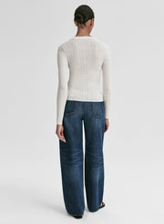 Woman wearing a white ribbed cardigan and blue jeans on a light gray background