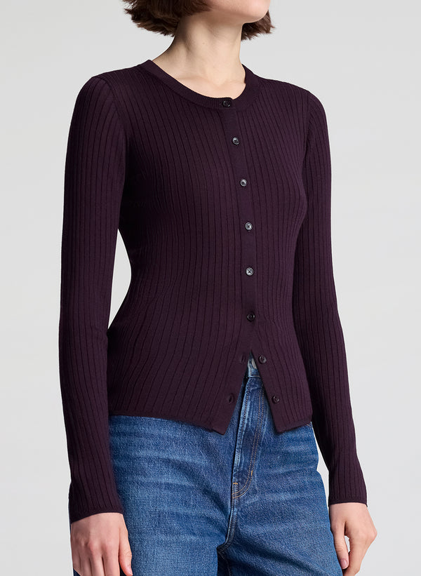 Person wearing a dark purple ribbed cardigan and blue jeans on a light gray background