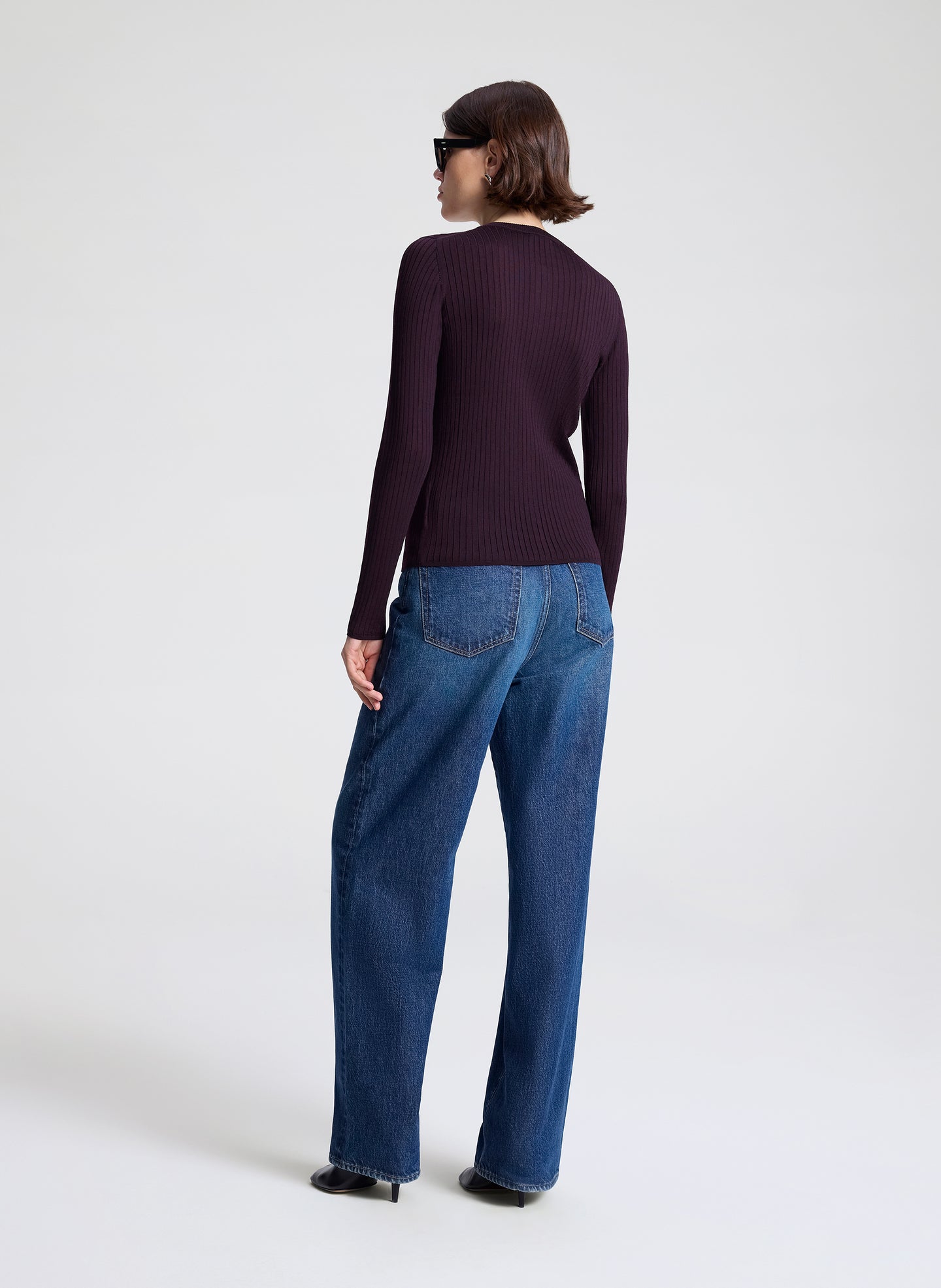 Person wearing a dark long-sleeve cardigan and blue jeans on a white background