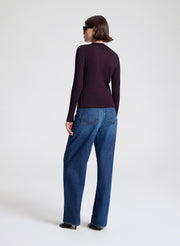 Person wearing a dark long-sleeve cardigan and blue jeans on a white background