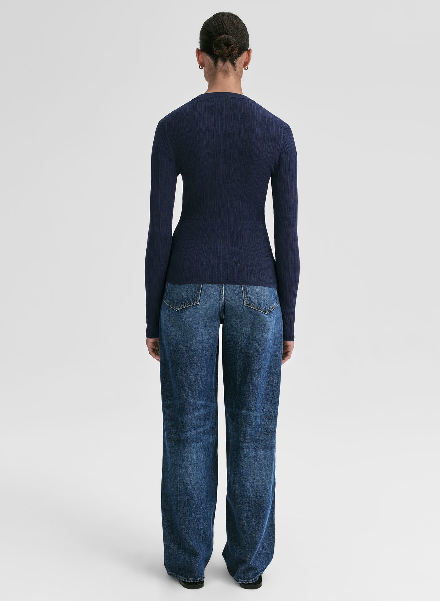 Person wearing a navy sweater and blue jeans on a white background