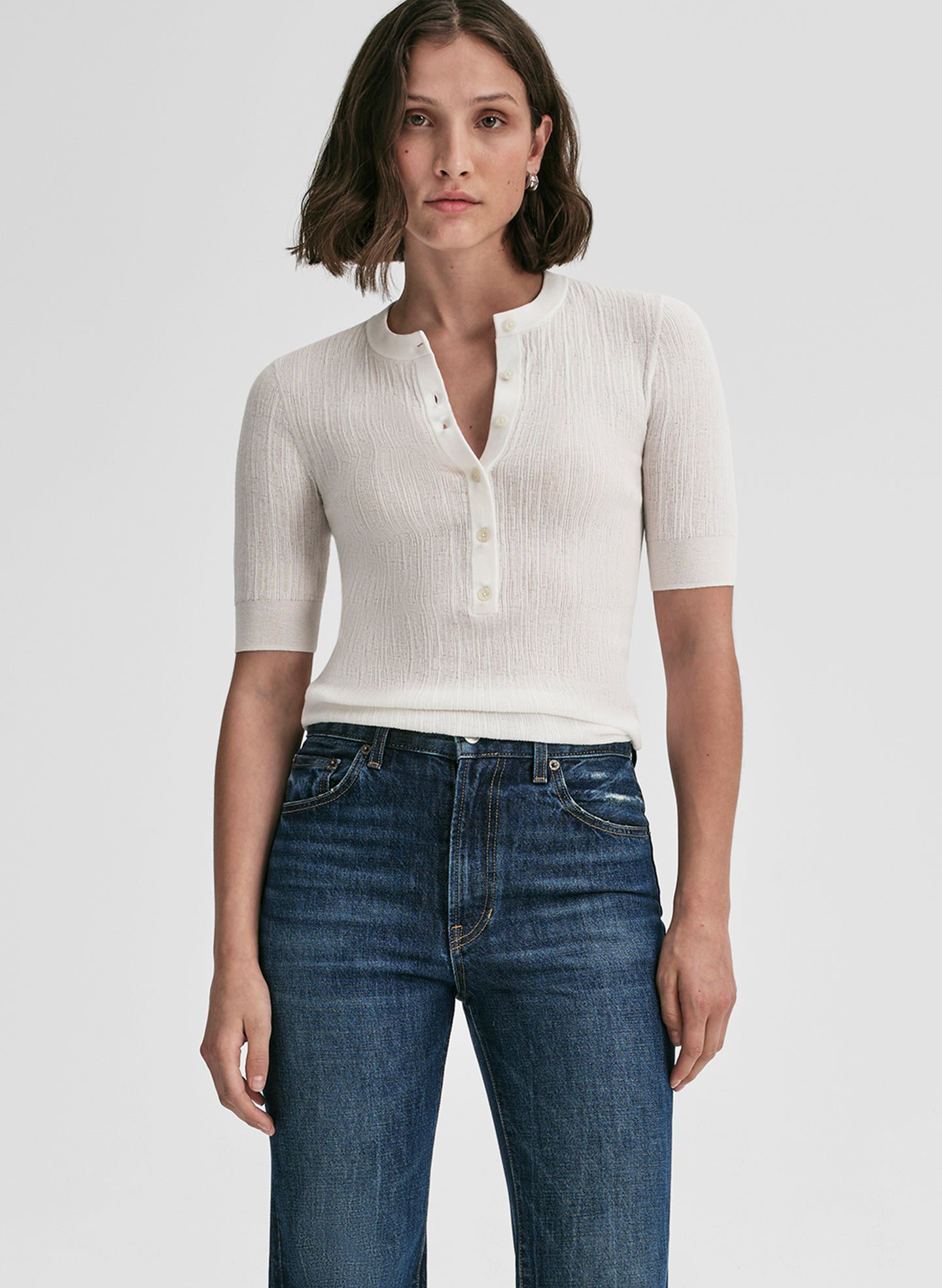 Woman wearing a white ribbed knit top and blue jeans on a light gray background
