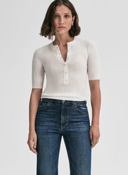 Woman wearing a white ribbed knit top and blue jeans on a light gray background