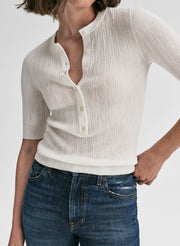 Person wearing a white ribbed knit shirt and blue jeans on a plain background