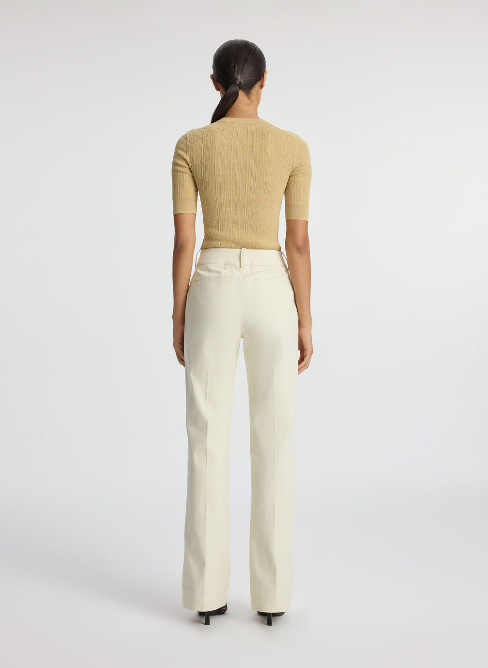 back  view of woman wearing beige half sleeve button placket shirt and cream pants