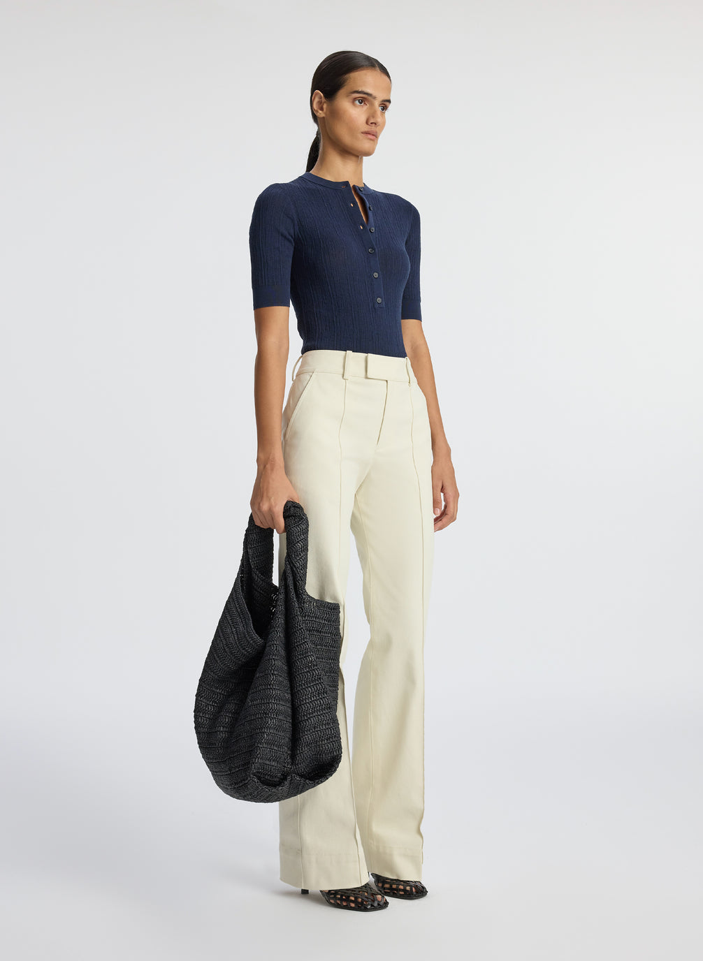 side view of woman wearing navy blue half sleeve button placket shirt and cream pants