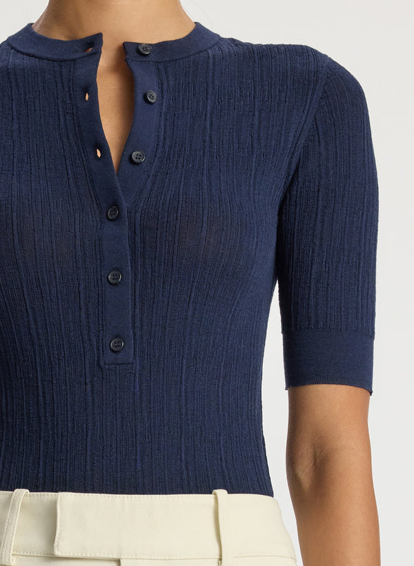 detail view of woman wearing navy blue half sleeve button placket shirt and cream pants