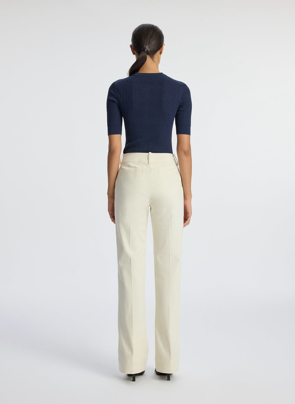 back view of woman wearing navy blue half sleeve button placket shirt and cream pants