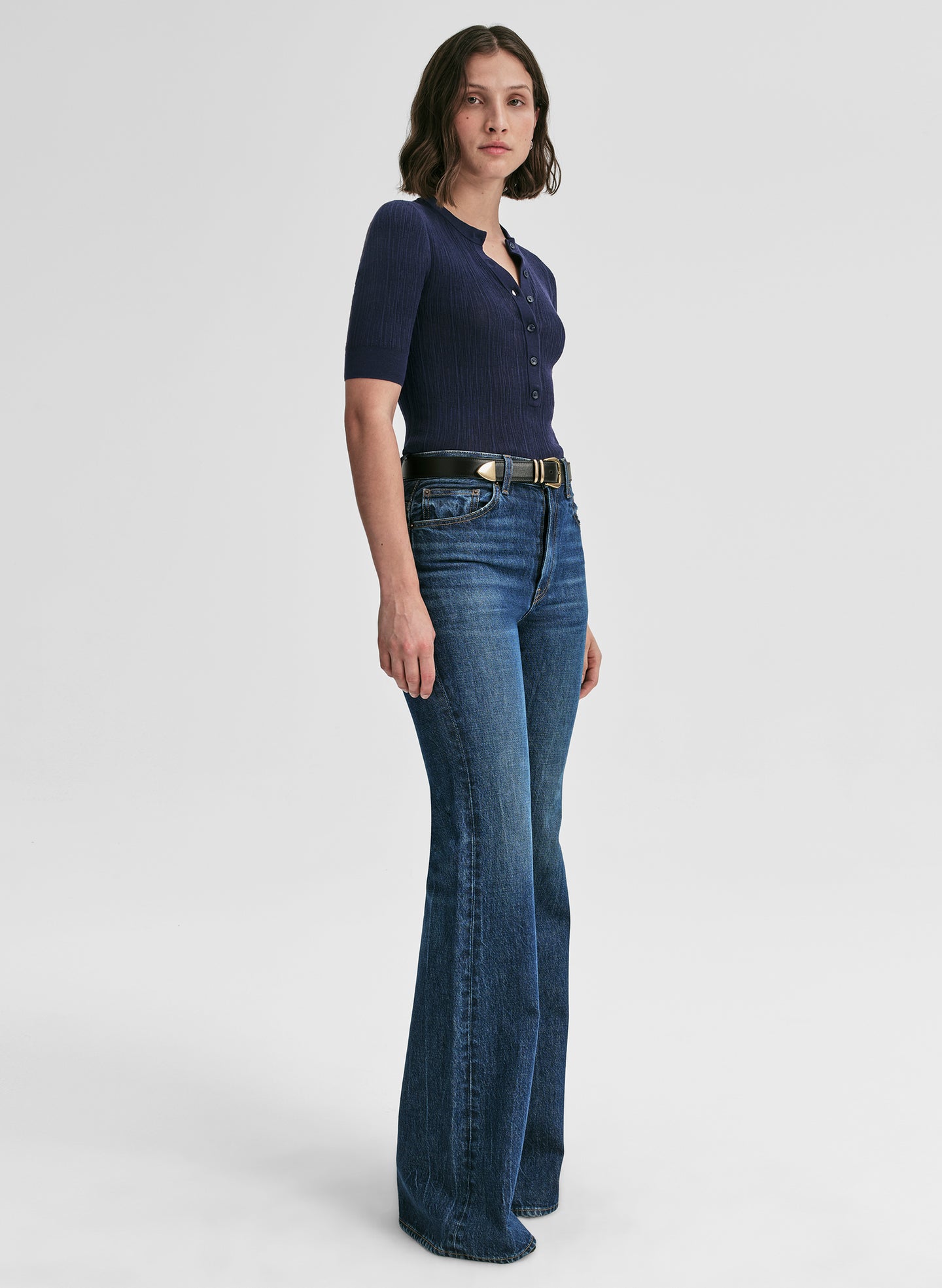 Woman wearing a navy blue shirt and blue jeans on a light gray background