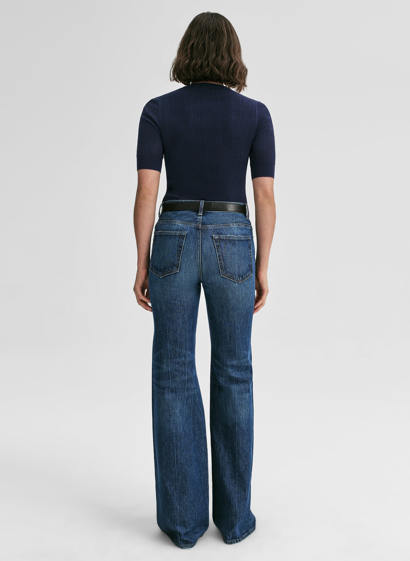 Person wearing blue jeans and a dark top on a white background