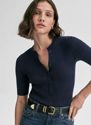 Woman wearing a navy ribbed top and jeans on a plain background