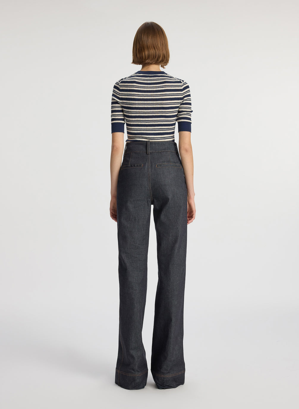 back  view of woman wearing navy blue striped half sleeve button placket shirt and dark wash raw denim jean