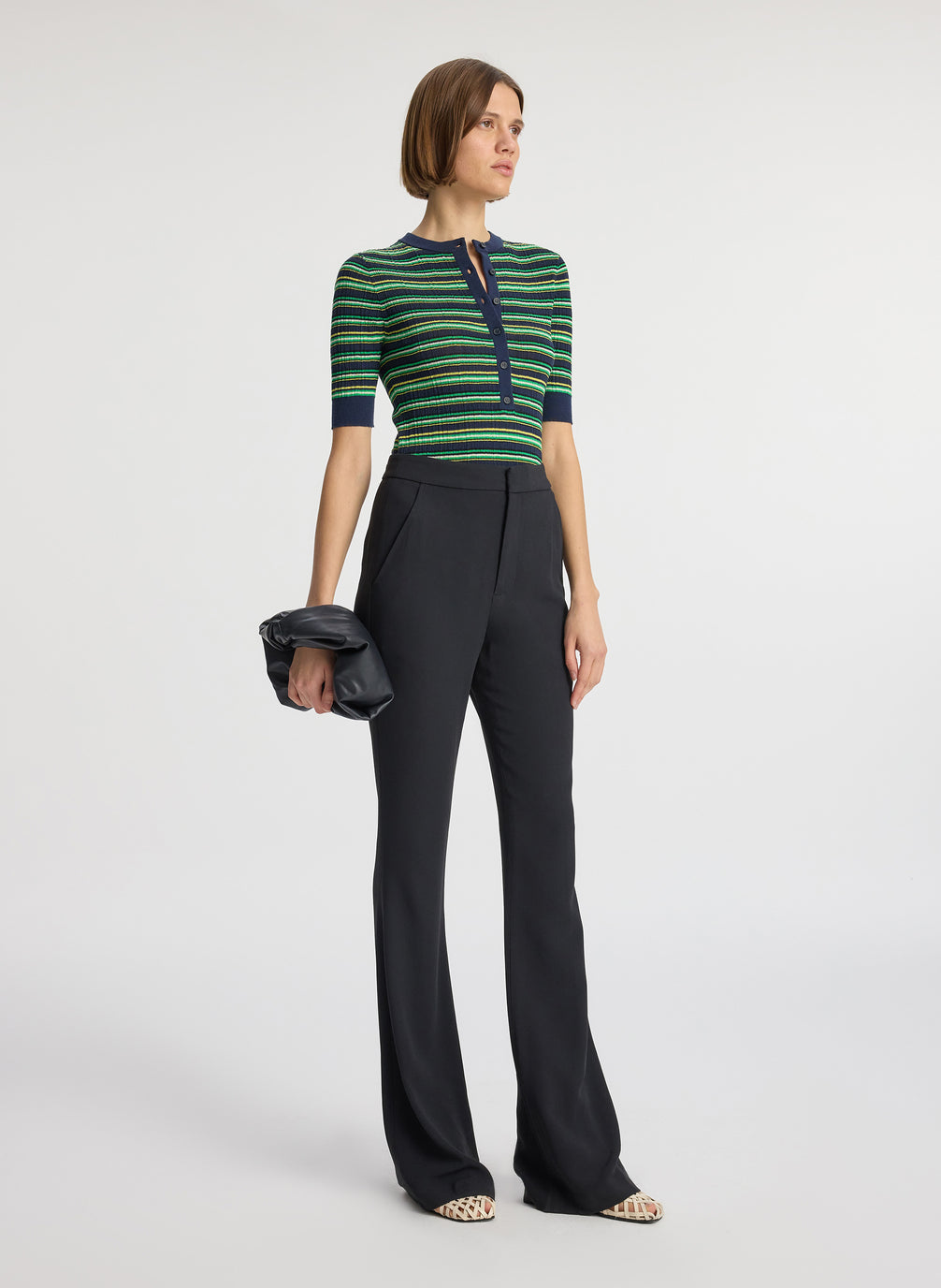 side view of woman wearing navy blue and green striped half sleeve button placket shirt and black pant